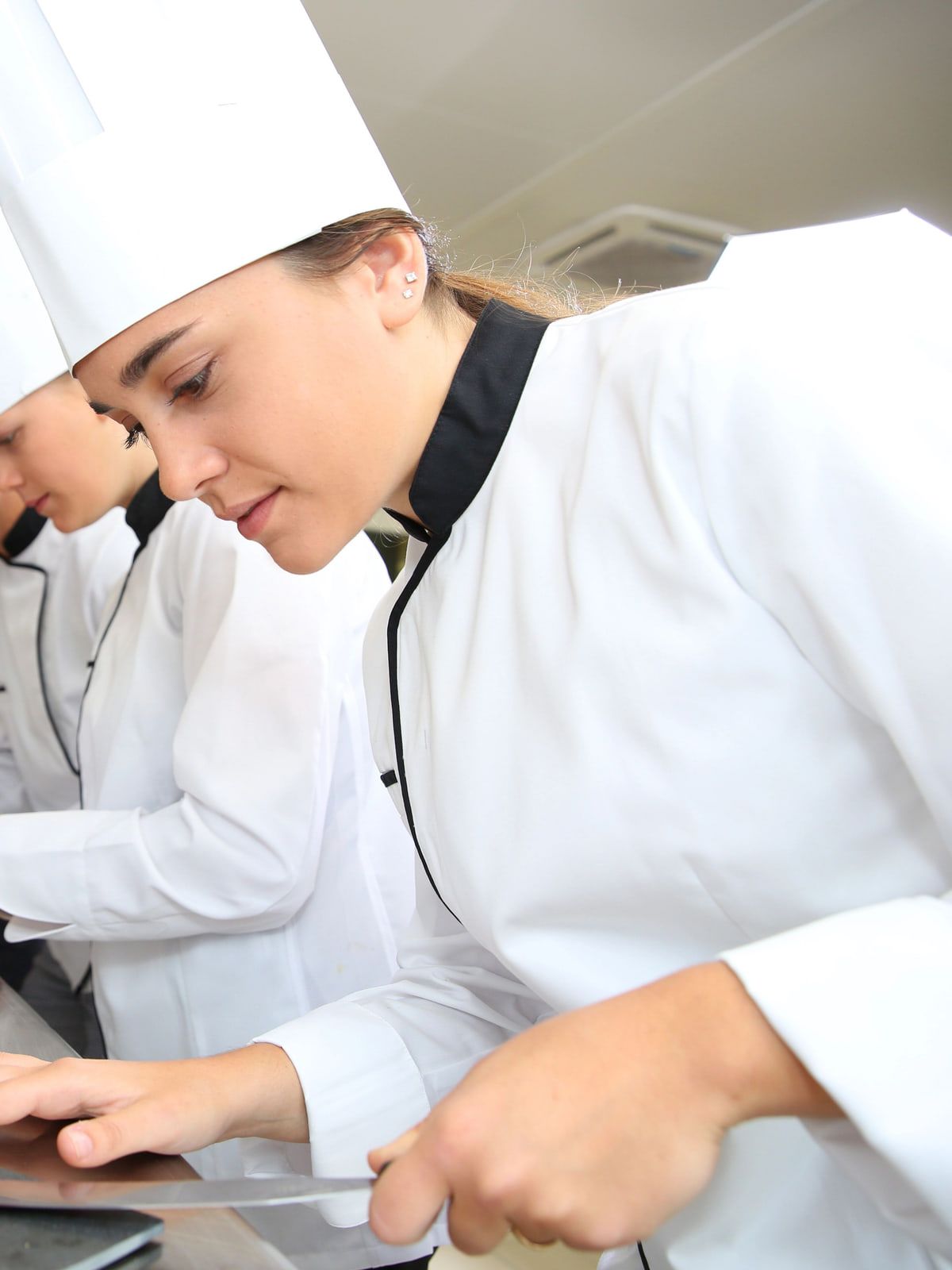 Cozinheiros de dólmã e toque blanche preparando pratos na cozinha profissional